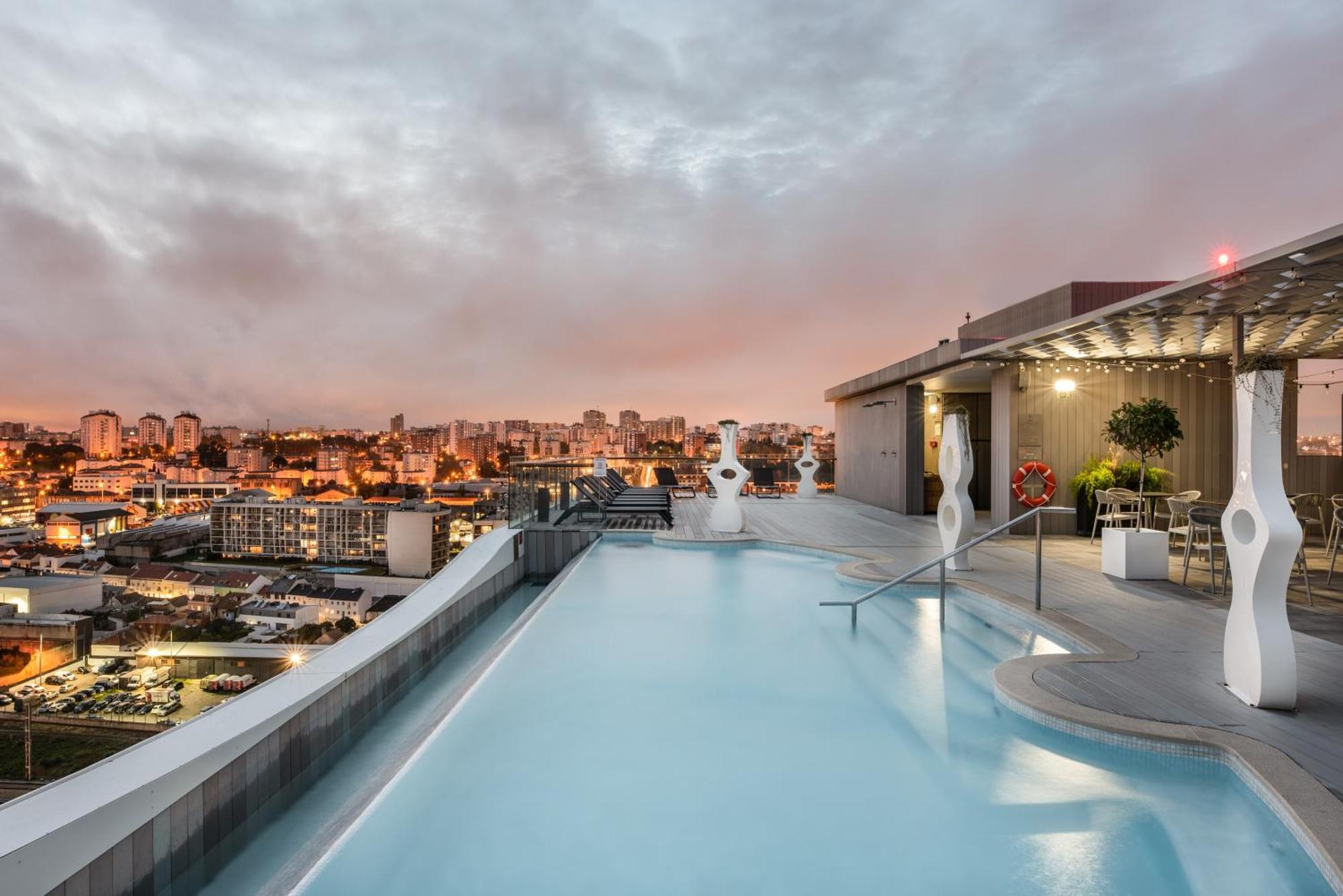 Eurostars Universal Lisboa 外观 照片 The photo shows a rooftop pool with a modern design, featuring clear blue water and a sleek edge that appears to blend into the skyline. In the background, there are city buildings illuminated by sunset colors, giving the scene a warm and inviting at