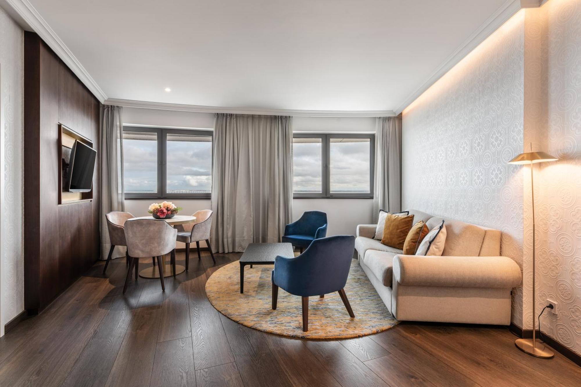 Eurostars Universal Lisboa 外观 照片 The photo shows a modern and stylish hotel room or suite. It features a comfortable sofa in a light color, accompanied by two accent chairs—one blue and one a neutral tone. There’s a coffee table in front of the seating area, and a round rug undernea