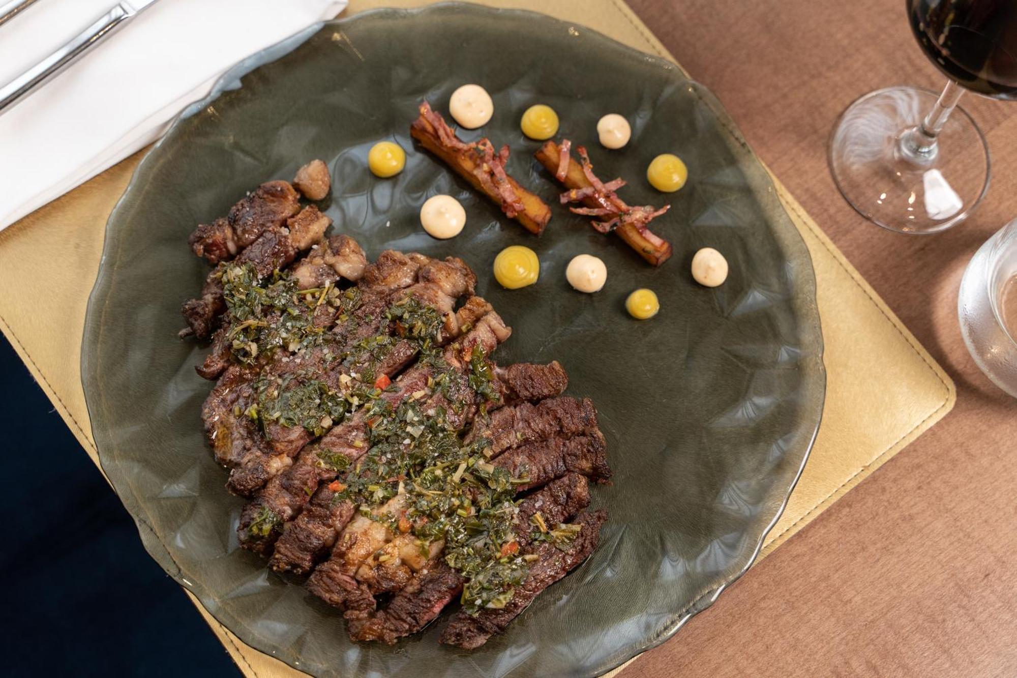 Eurostars Universal Lisboa 外观 照片 The photo shows a plated dish featuring a serving of sliced steak that appears to be seasoned with herbs or spices. The steak is arranged on a dark green, textured plate. Accompanying the steak are small dollops of sauces and a few pieces that resemb