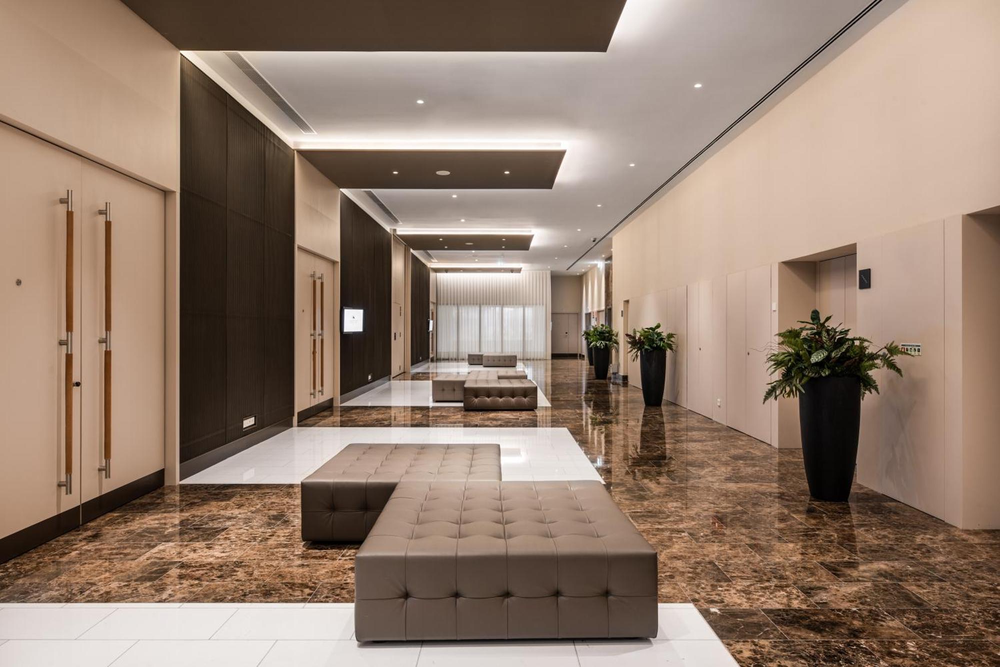Eurostars Universal Lisboa 外观 照片 The photo depicts a modern lobby or reception area. The space features polished marble flooring that contrasts with dark wood paneling on the walls. There are multiple low benches with tufted upholstery arranged in the area. Tall plants in black pots