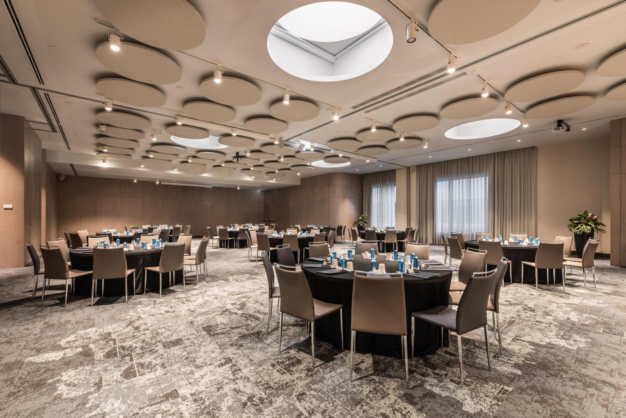 Eurostars Universal Lisboa 外观 照片 The photo shows a spacious banquet room or conference hall. There are several round tables set up, each covered with black tablecloths and featuring light blue decorations or tableware. The room has a modern design, with a beige and soft gray color p